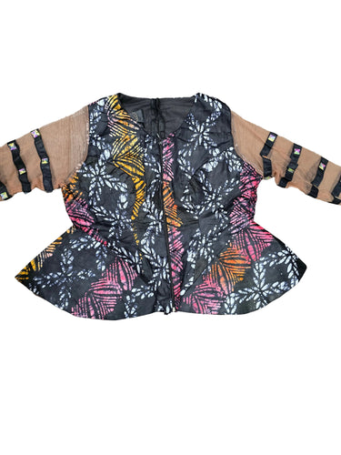 A women's sleeveless corset-style top with a black base and a vibrant batik-style floral pattern in pink, orange, yellow, and white, featuring beige underarm panels with black strappy details, laid flat on a gray wood floor.