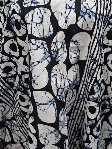 A black and white patterned kaftan dress with blue tie-dye accents, draped on a white mannequin torso in a kitchen setting.