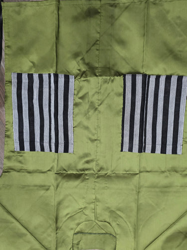 An olive green garment laid flat on a wooden floor, featuring two rectangular panels with black and white vertical stripes on the sides.