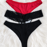Three pairs of women's bikini-style underwear laid flat on a white faux-fur surface: a red pair at the top, a black lace-trim pair in the middle, and a solid black pair at the bottom.
