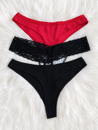 Three pairs of women's bikini-style underwear laid flat on a white faux-fur surface: a red pair at the top, a black lace-trim pair in the middle, and a solid black pair at the bottom.
