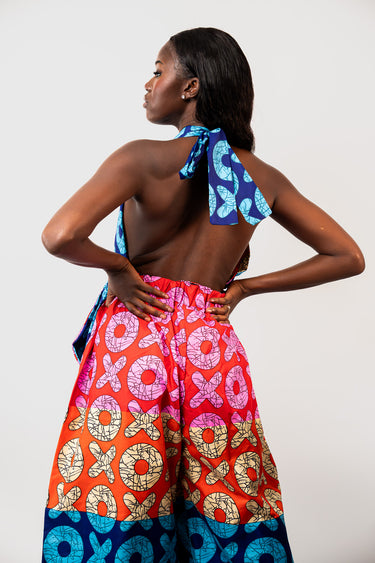 A woman shown from the back wearing a colorful patterned halter top and wide-leg pants set. The fabric features vibrant red, orange, blue, pink, and beige circular and cross-like patterns.