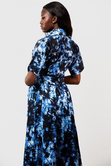 A woman shown from the back wearing a short-sleeve collared dress with a blue and black tie-dye pattern, photographed against a plain light gray studio background.