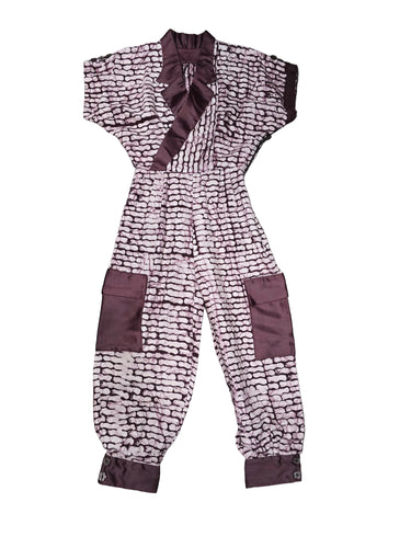 A one-piece long-sleeve jumpsuit with a pink and white abstract pattern and dark brown trim, laid flat on a gray wood floor.