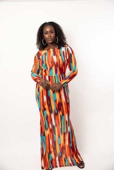 A woman modeling a long-sleeve maxi dress with a vibrant vertical ikat-style pattern in orange, red, yellow, blue, and white, standing against a plain white studio background.