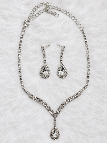 Silver-tone rhinestone necklace and matching drop earrings laid flat on a white faux fur background.