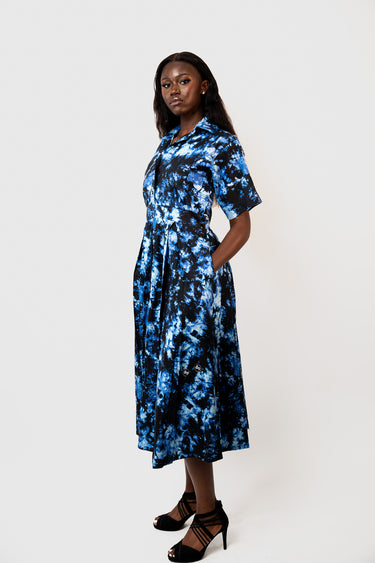A woman modeling a short-sleeve midi dress with a blue and black abstract floral print, standing against a plain white studio background.