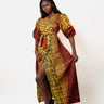 A woman modeling a long African wax print dress with puff sleeves and a high leg slit, featuring a vibrant yellow, red, and black pattern, set against a plain white studio background.