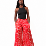 A model stands against a white background wearing red wide-leg pants with a white geometric pattern, a black sleeveless top, and white sneakers.