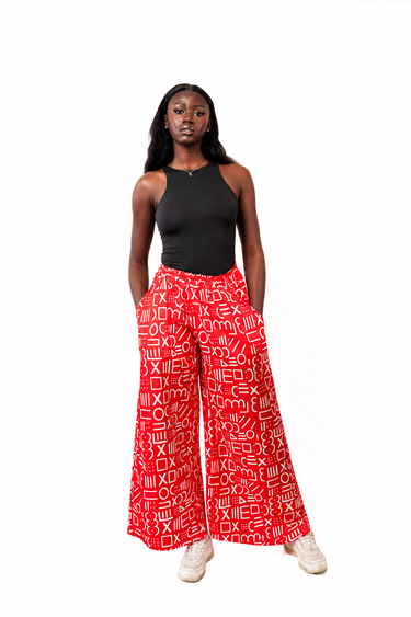 A model stands against a white background wearing red wide-leg pants with a white geometric pattern, a black sleeveless top, and white sneakers.